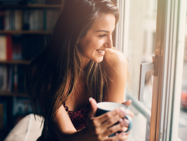 Woman holding a mug by a window reflecting calmly