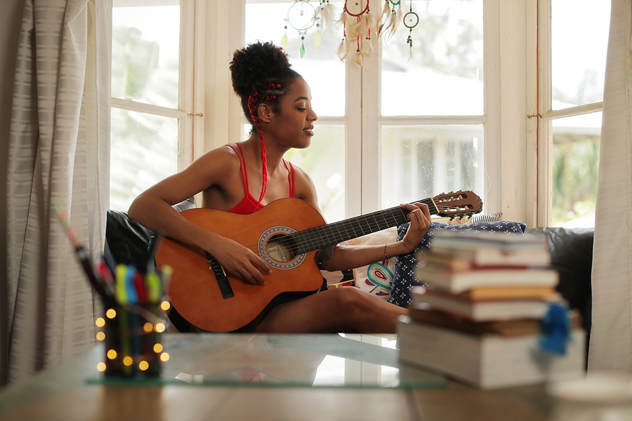 Woman playing guitar indoors expressing creativity and emotional regulation
