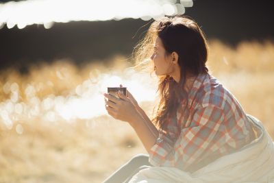Woman sitting outdoors holding a mug and reflecting quietly in nature